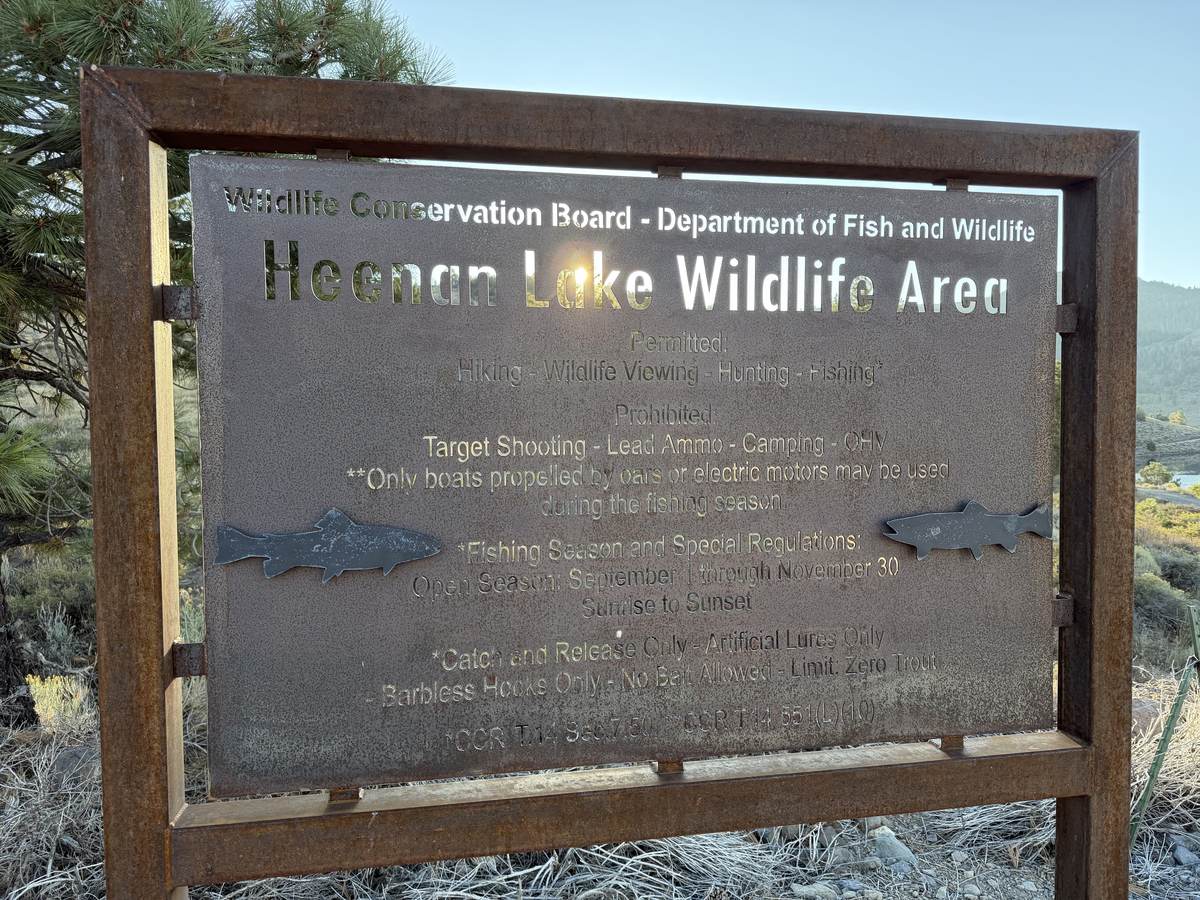 A weathered steel sign with two cut-steel trout: Wildlife Conservation Board, Department of Fish and Wildlife, Heenan Lake Wildlife Area, and below it the permitted uses and the fishing season.